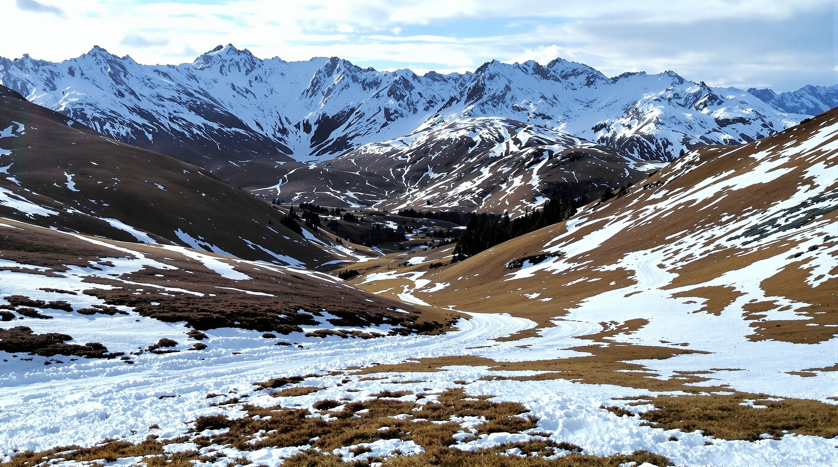 Vue d'une piste de ski peu enneigée en basse altitude aux Menuires, avec des zones d'herbe visible sur les bords, typique de début ou fin de saison.